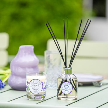 Diffuser and  floral, woody iris candle on a table with blurred greenery in the background