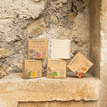 Durance Pine & Olive wood Soap  bars and packaging on a stone surface with a stone wall background