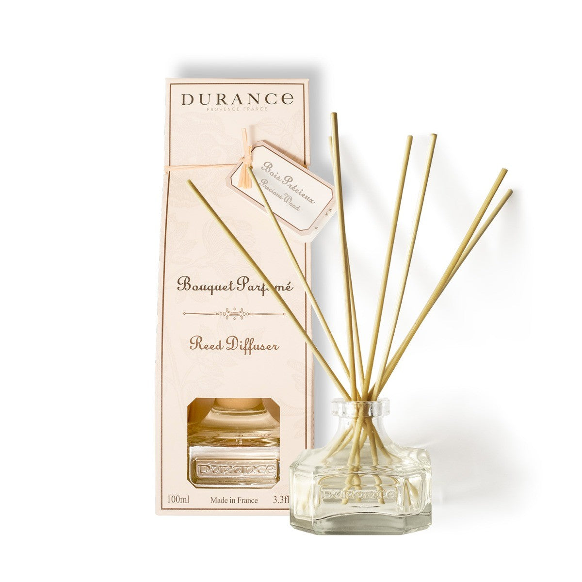 A Durance branded scented bouquet Precious Wood Diffuser 100 mlwith several gold-colored sticks, a clear glass vase, and a pink cardboard box.