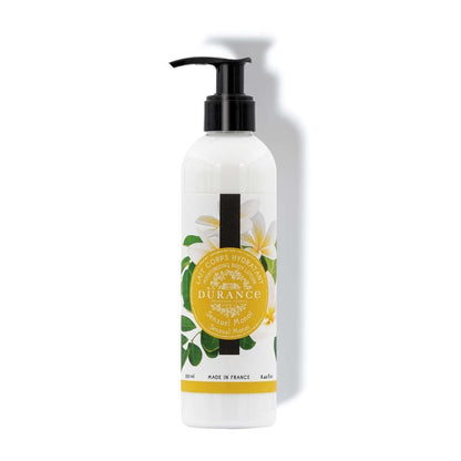A white pump bottle with a label that has the brand 'Durance' and the product name 'Sensual Monoi'. There are images of flowers and leaves, and the text indicates the product is a moisturizing body lotion.