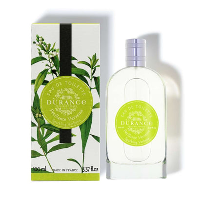 A bottle of Durance sparkling verbena eau de toilette perfume next to its packaging box, both featuring a green label with images of verbena leaves 
